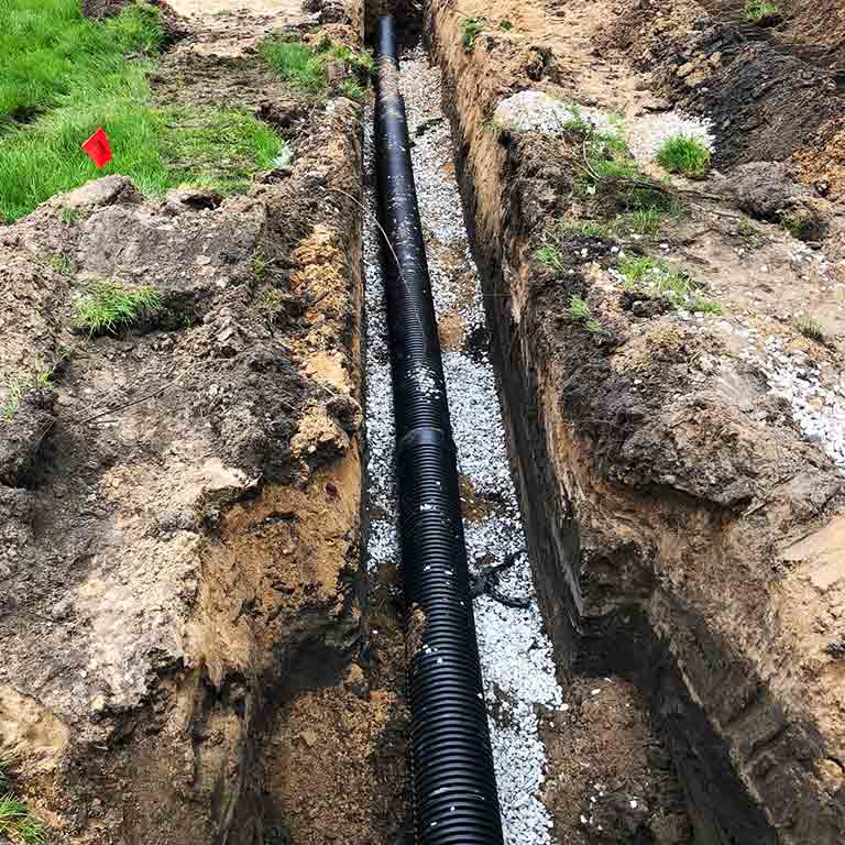 A black pipe lays in a trench in the ground.